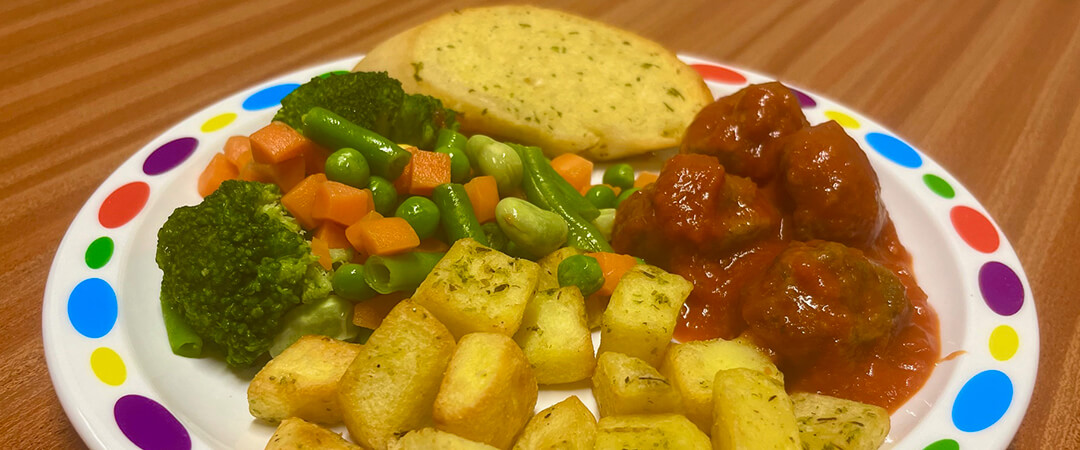 Beef meatballs in tomato sauce served with diced potatoes, seasonal vegetables and garlic bread