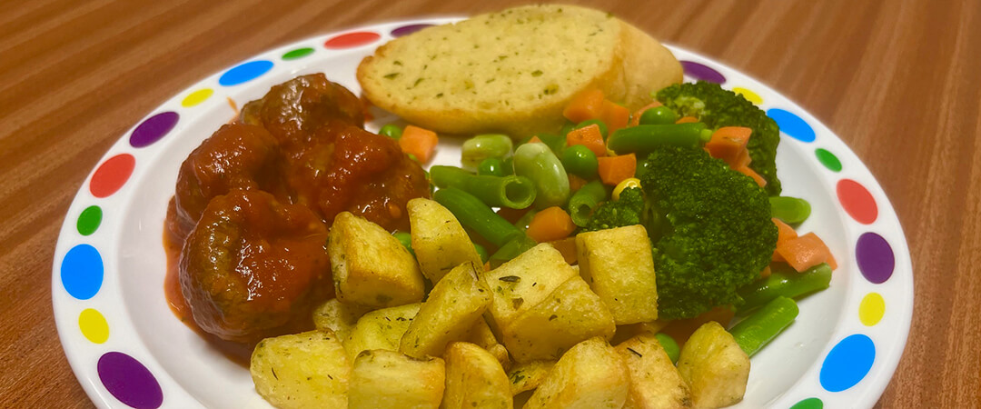 Veggie meat-free balls (Ve) in tomato sauce served with diced potatoes, seasonal vegetables and garlic bread