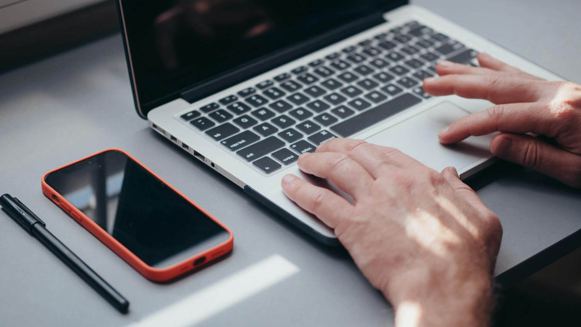 A person using a laptop with a smart phone on the desk next to them (Pexels - kindelmedia)