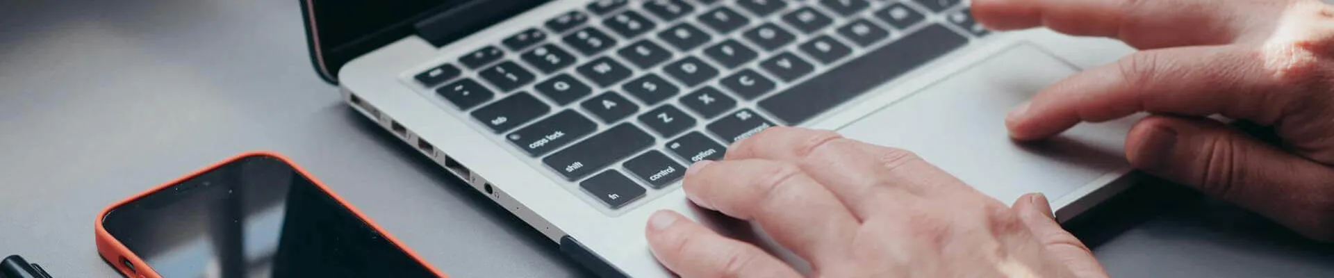 A person using a laptop with a smart phone on the desk next to them (Pexels - kindelmedia)