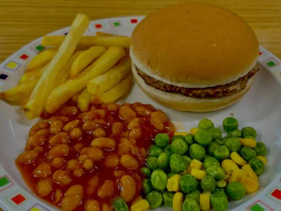 Beefburger in a roll or bread and spread served with chips, peas and sweetcorn or baked beans