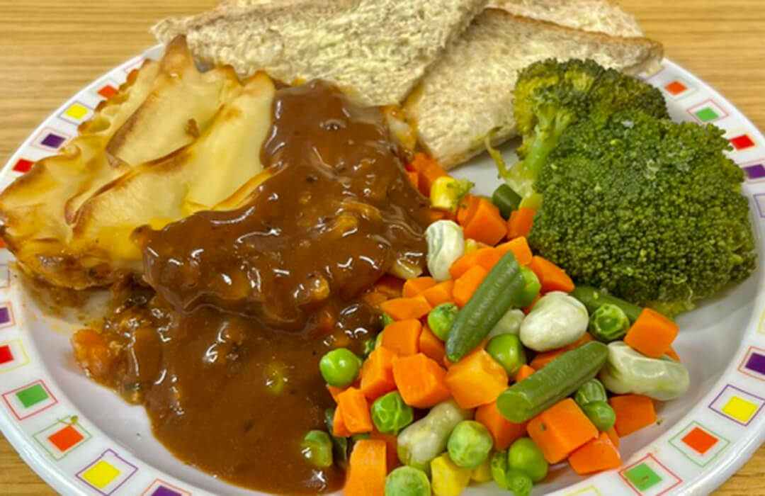 Cottage pie served with mixed vegetables, broccoli, gravy and bread and spread