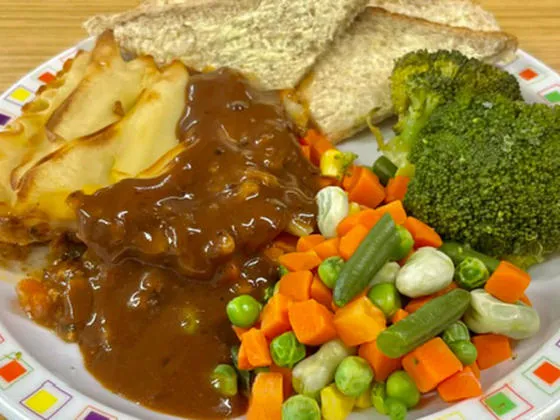 Cottage pie served with mixed vegetables, broccoli, gravy and bread and spread
