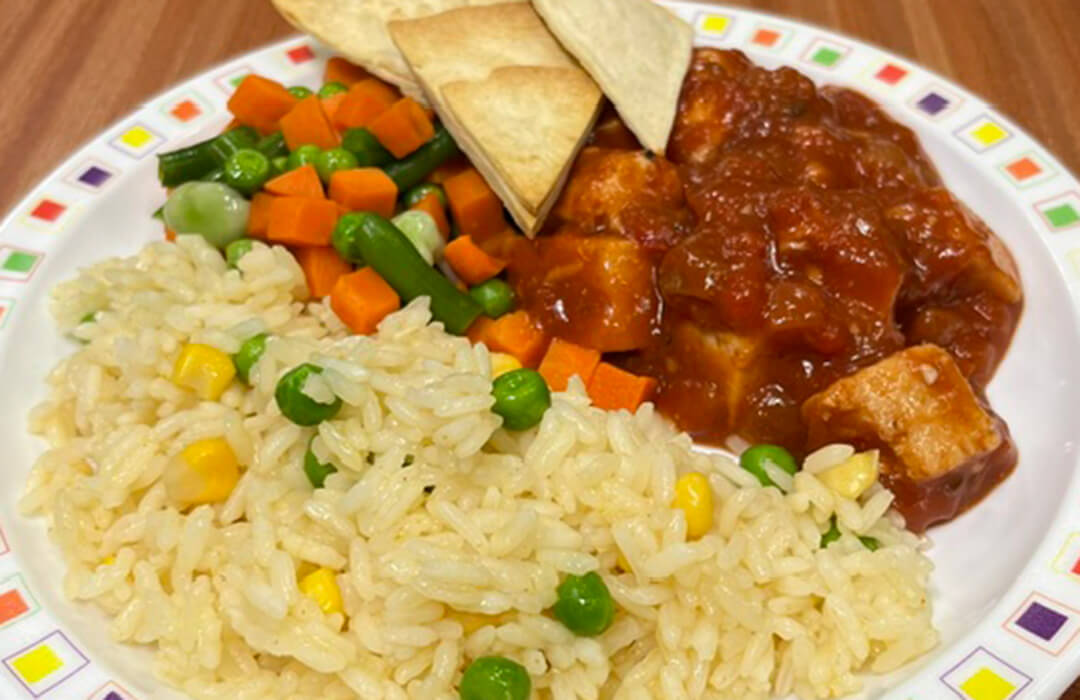 Homemade BBQ chicken served with vegetable rice, tortilla chips, peas and mixed vegetables