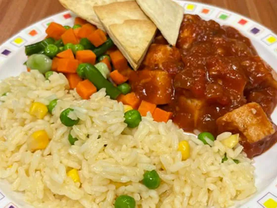 Homemade BBQ chicken served with vegetable rice, tortilla chips, peas and mixed vegetables