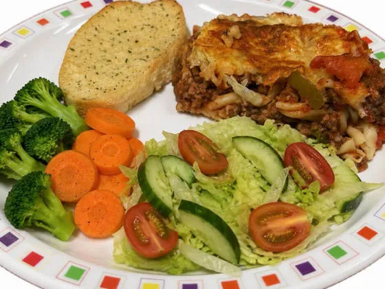 Homemade lasagne served with garlic bread, salad, broccoli and carrots