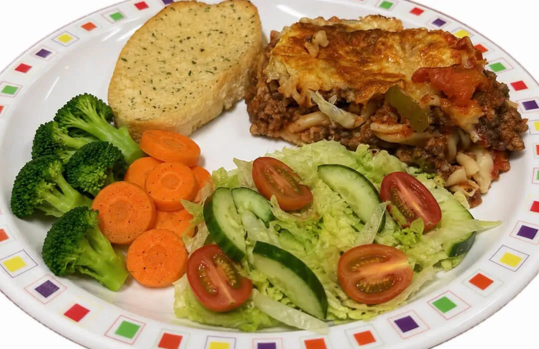 Homemade lasagne served with garlic bread, salad, broccoli and carrots