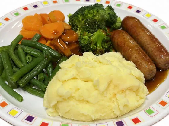 Pork sausage served with mashed potato, carrots, broccoli and gravy