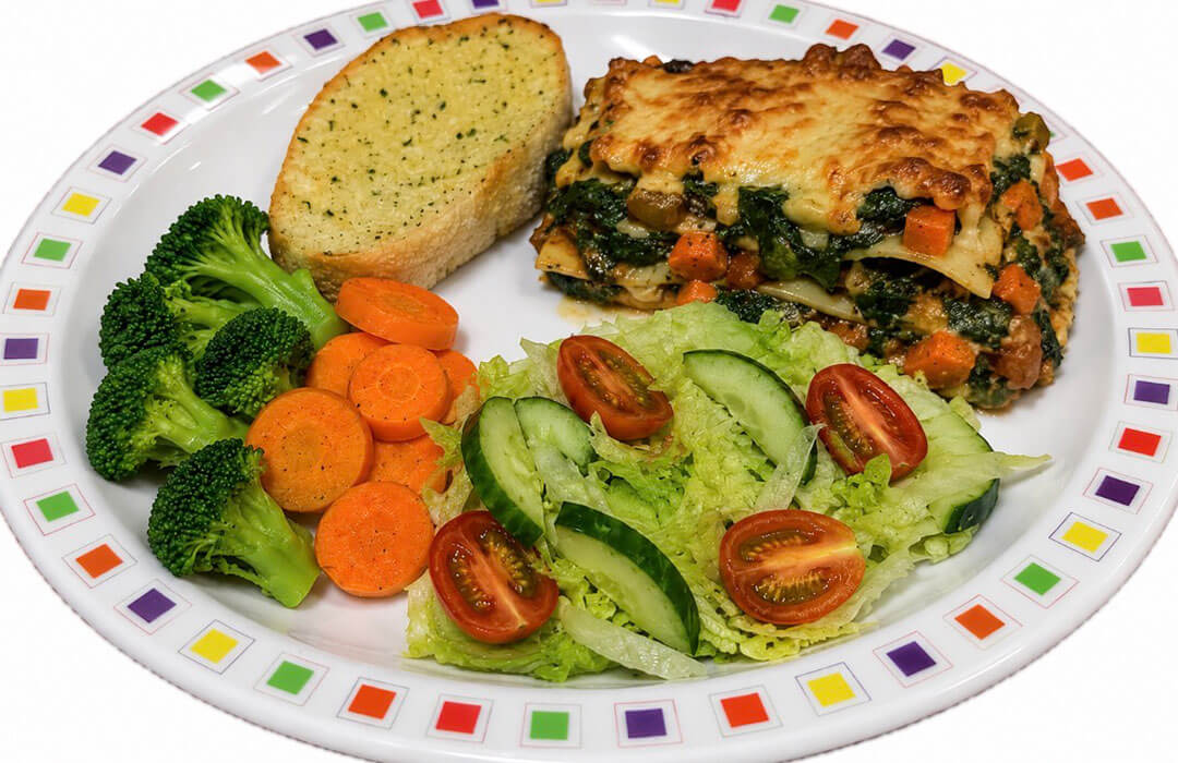 Spinach and vegetable lasagne (V) served with garlic bread, salad, broccoli and carrots