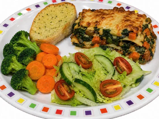 Spinach and vegetable lasagne (V) served with garlic bread, salad, broccoli and carrots