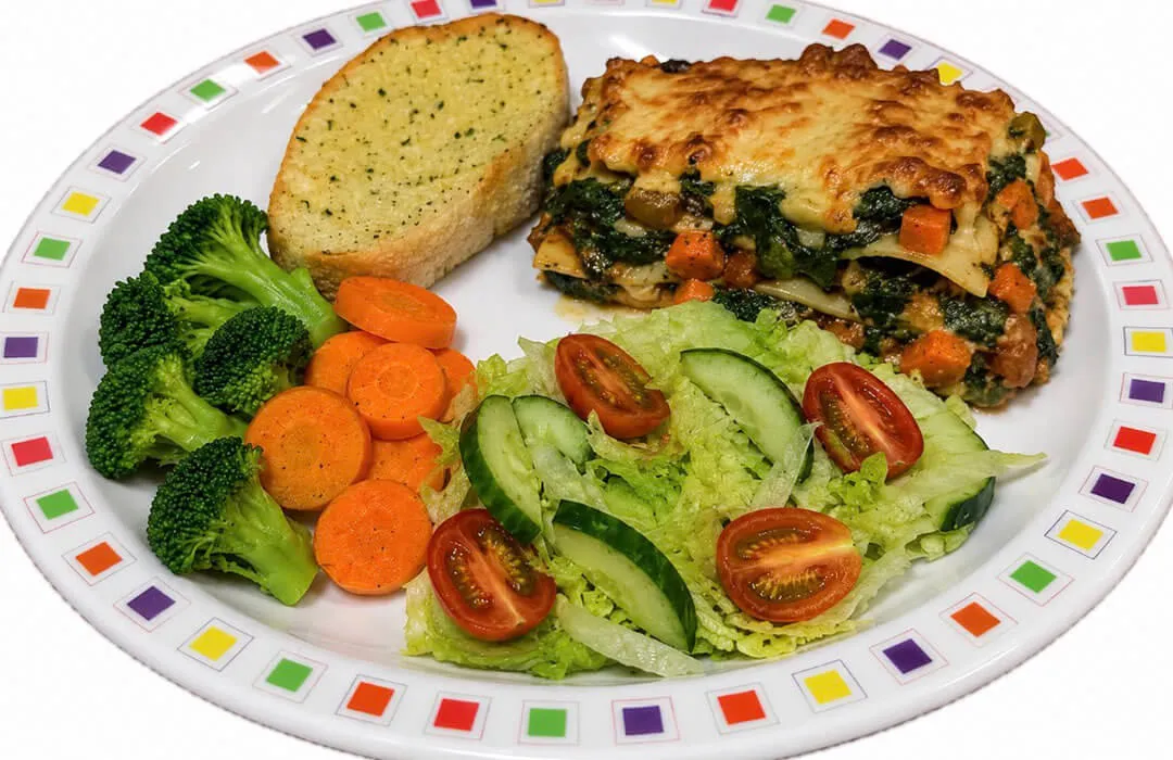 Spinach and vegetable lasagne (V) served with garlic bread, salad, broccoli and carrots