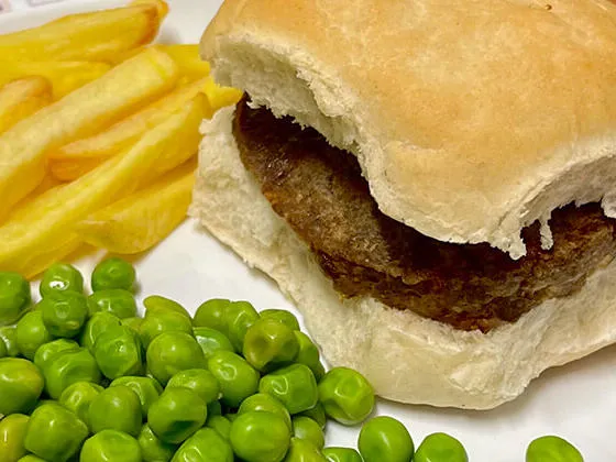 Beefburger in a bun served with chips and peas