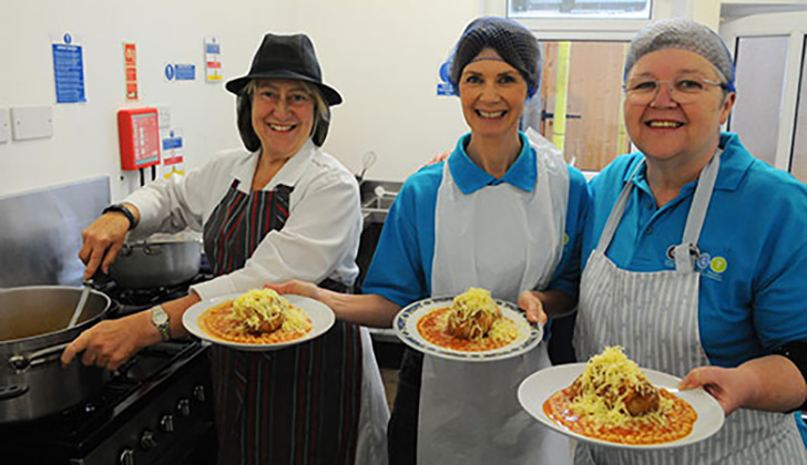 Catering staff holding plates with jacket potatoes covered in cheese and beans