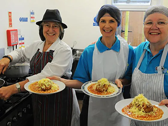 Catering staff holding plates with jacket potatoes covered in cheese and beans