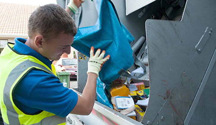 A member of the recycling team emptying a blue bag into the recycling lorry