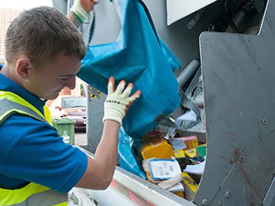 A member of the recycling team emptying a blue bag into the recycling lorry