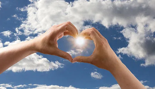 Hands forming the shape of a heart with the sun shining through