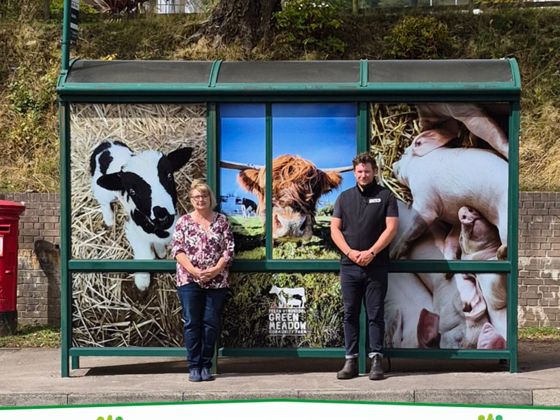 Cllr Owen and Greenmeadow Community Farm manager Jac Griffiths standing outside a bus stop which has been wrapped in farm animal imagery