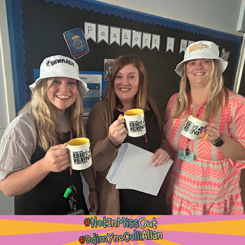 Three woman smiling holding mugs and wearing hats promoting the Urdd Eisteddfod Bro'r Wenynen Gwent